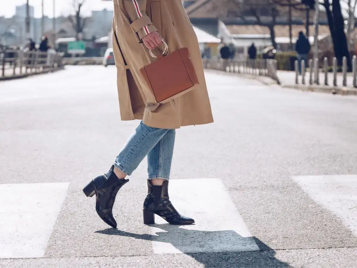 Kobieta w płaszczu i jeansach przechodzi przez pasy, prezentując stylowe botki skarpetkowe. Idealne botki skarpetkowe stylizacje na co dzień.
