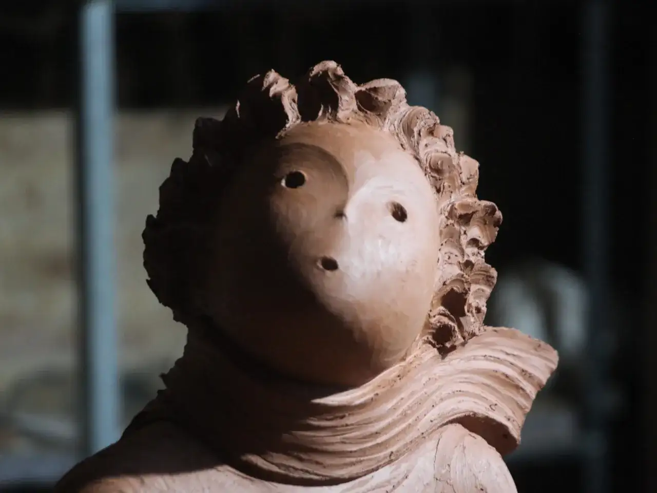 Ton-Skulptur eines Kopfes mit welligem Haar und zwei Augenlöchern.