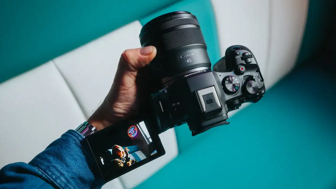 Dłoń trzyma zaawansowany **canon aparat lustrzanka** z obiektywem RF 45mm. Na ekranie widoczny jest podgląd ujęcia.