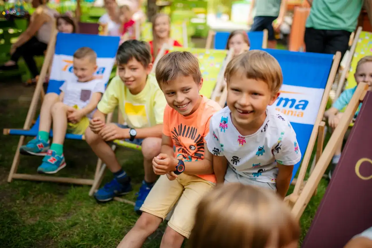 Uśmiechnięte dzieci siedzą na leżakach w parku. To idealne miejsce na letnie zabawy, jak w najlepszych parkach dla dzieci.