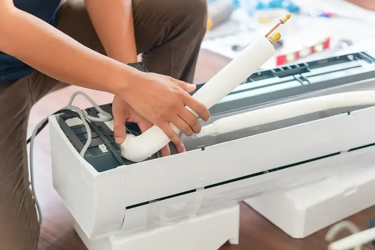 Ręce montują białą jednostkę klimatyzacyjną, przygotowując ją do samodzielnego montażu klimatyzacji.