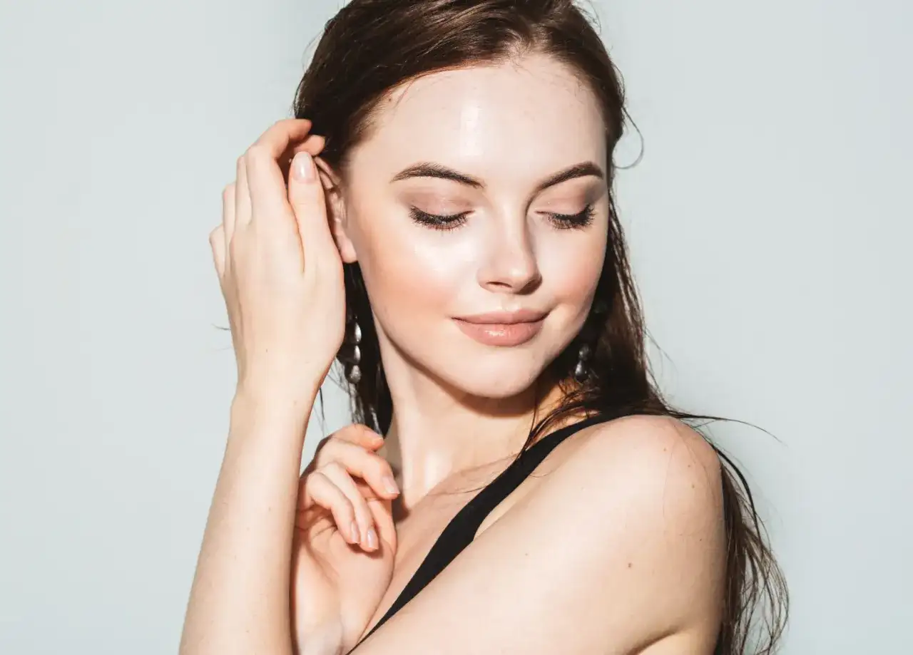 Portret kobiety z zamkniętymi oczami, dotykającej włosów, z widocznymi sztucznymi rzęsami.