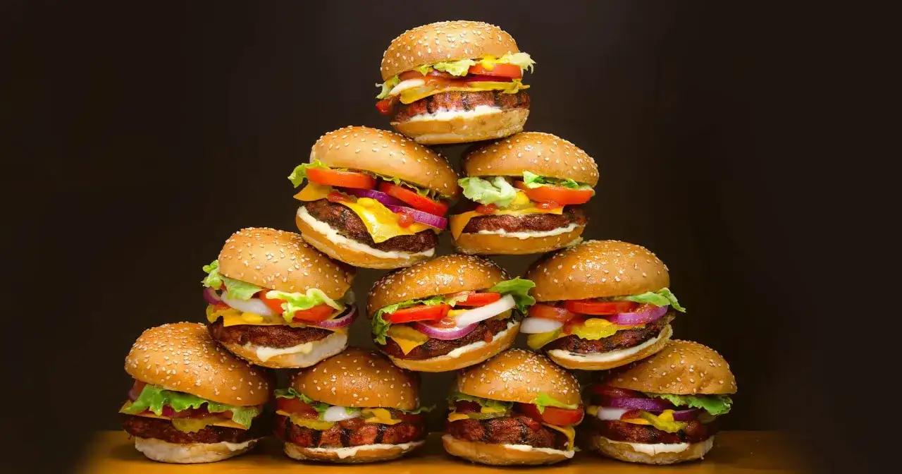 Stos pysznych domowych hamburgerów z sezamem, serem, sałatą i warzywami.