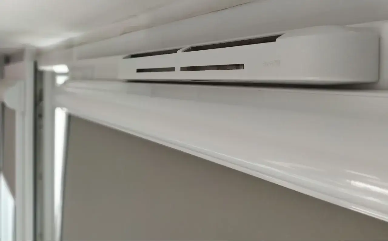 Biały nawiewnik okienny z logo "Aira HY". Dowiedz się, jak zamknąć wywietrzniki w oknach, aby zapewnić komfort termiczny.