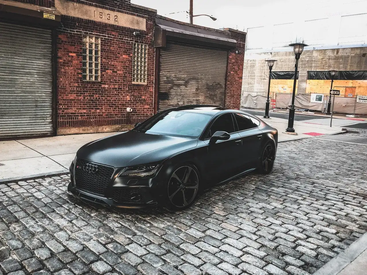 Matowy czarny Audi RS7 na brukowanej ulicy przed ceglanym budynkiem.