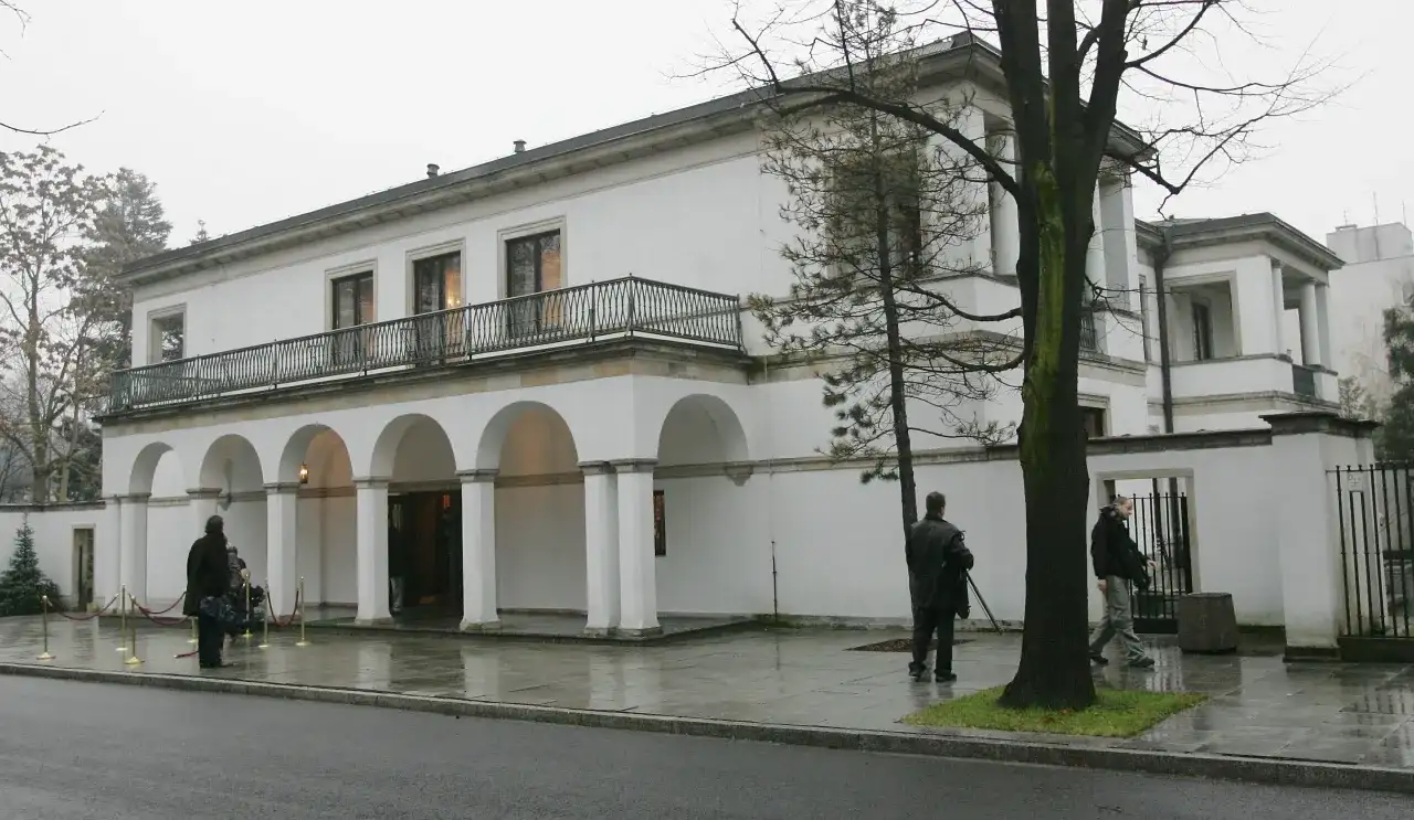 Biała willa z arkadami, gdzie mieszka Donald Tusk. Na zewnątrz widać kilka osób i drzewa.