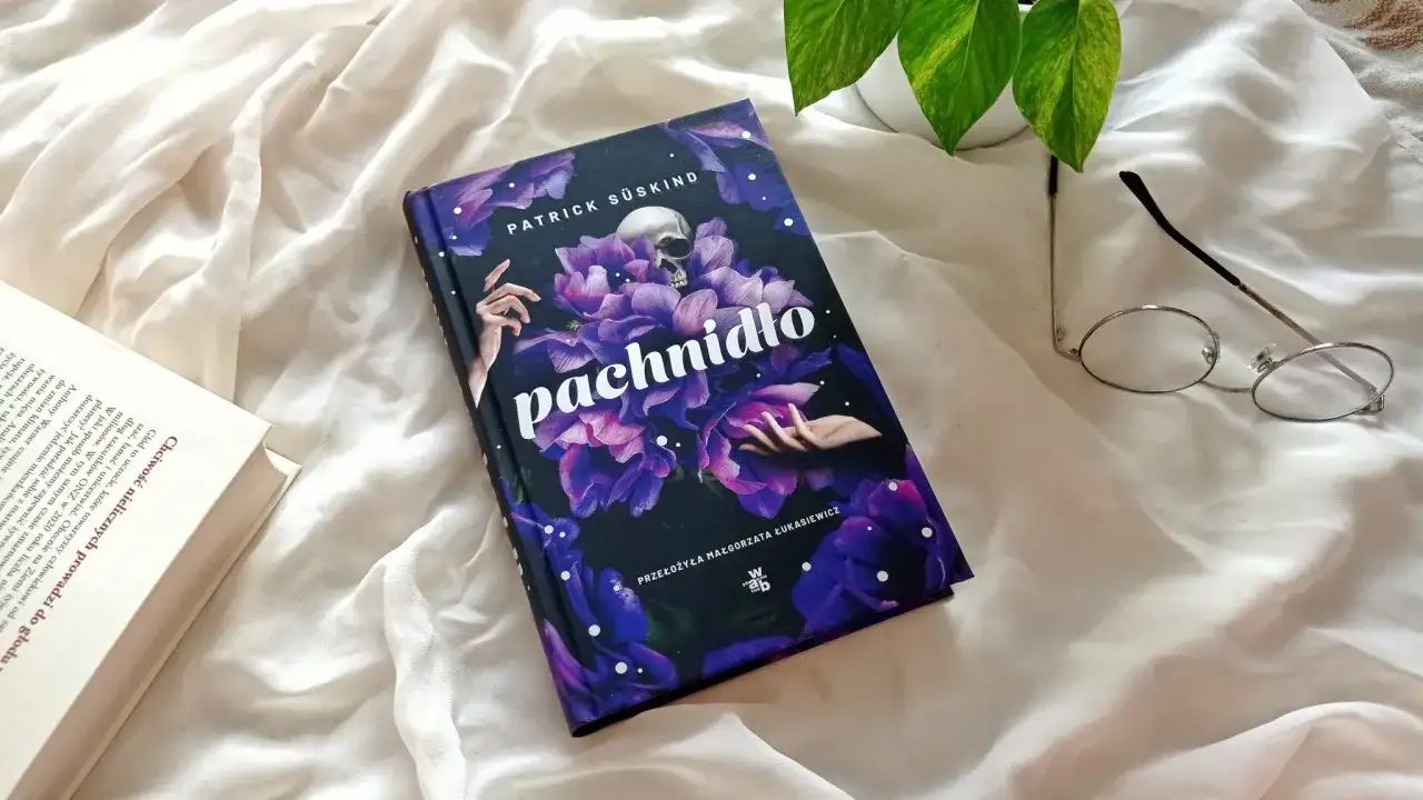 Recenzja książki "Pachnidło" Patricka Süskinda. Na zdjęciu okładka z czaszką i kwiatami, obok okulary i otwarta książka.