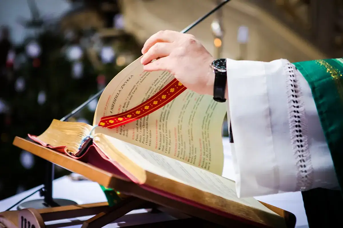 Dłoń księdza przewracająca kartki księgi liturgicznej na pulpicie.