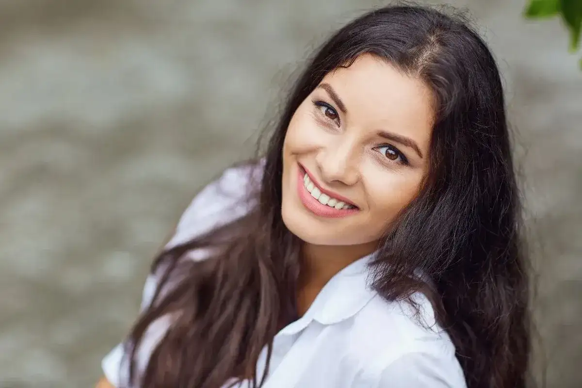 Uśmiechnięta kobieta o ciemnych włosach w białej koszuli.