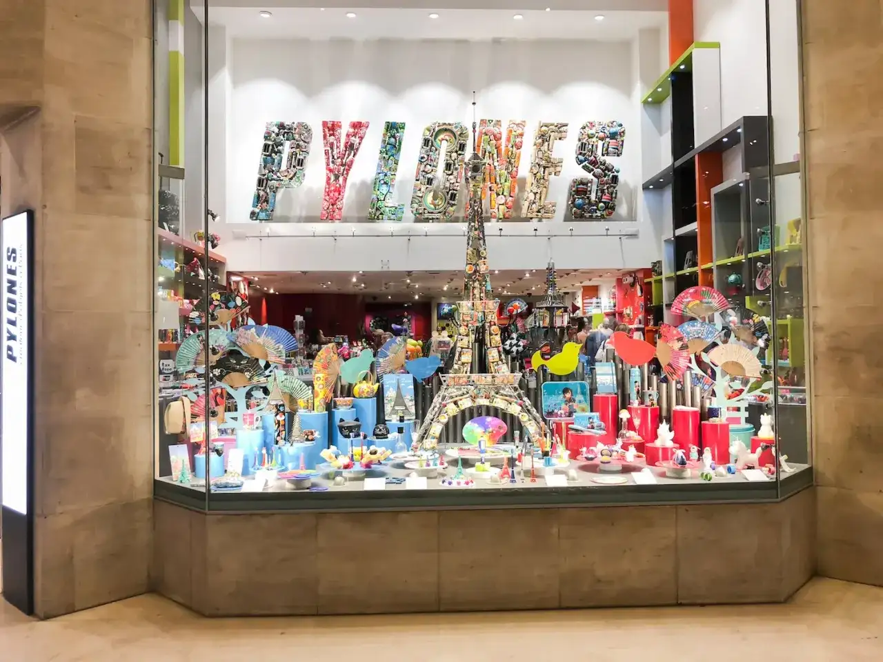 Kolorowa witryna sklepu PYLONES w Paryżu. Znajdziesz tu mnóstwo pomysłów, co kupić w Paryżu: wachlarze, wieże Eiffla, figurki i inne gadżety.