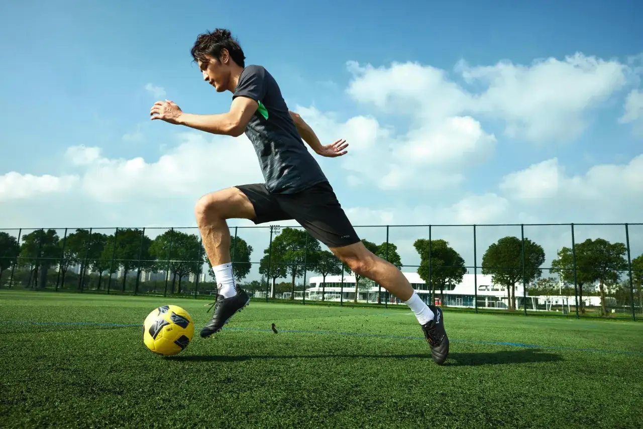 Piłkarz w ruchu kopie żółtą piłkę na zielonym boisku pod błękitnym niebem.