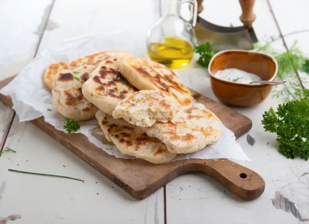 Stos chlebków naan na desce, obok miseczki z sosem i oliwy.