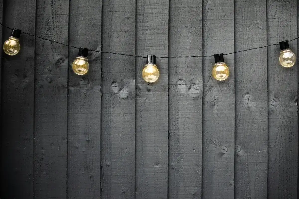 Ciepłe światło girlandy żarówkowej na ciemnej, drewnianej desce. Idealny pomysł, jaki kabel do oświetlenia ogrodu, by stworzyć przytulną atmosferę.