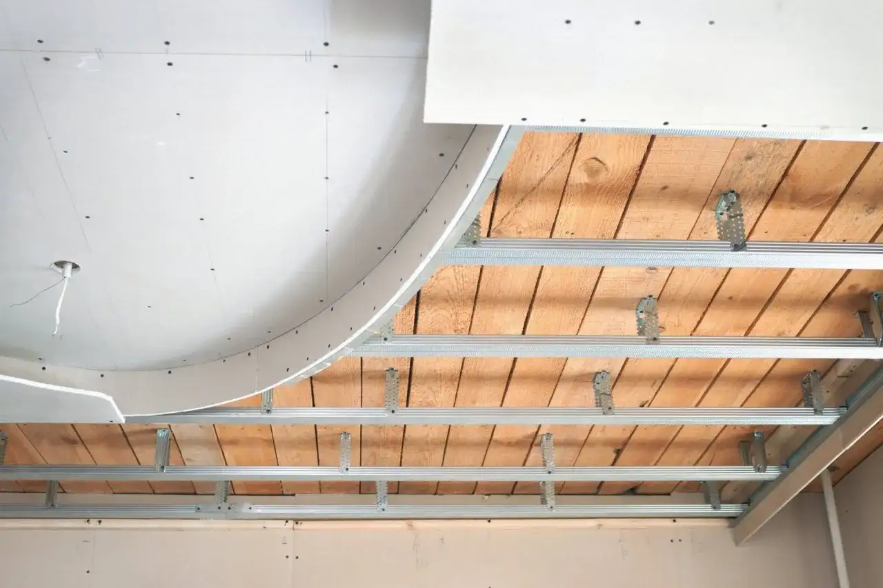 Montaż sufitu podwieszanego z płyt gipsowo-kartonowych. Widać drewniany strop i metalowy stelaż, który posłuży do zamontowania oświetlenia, np. halogenów.