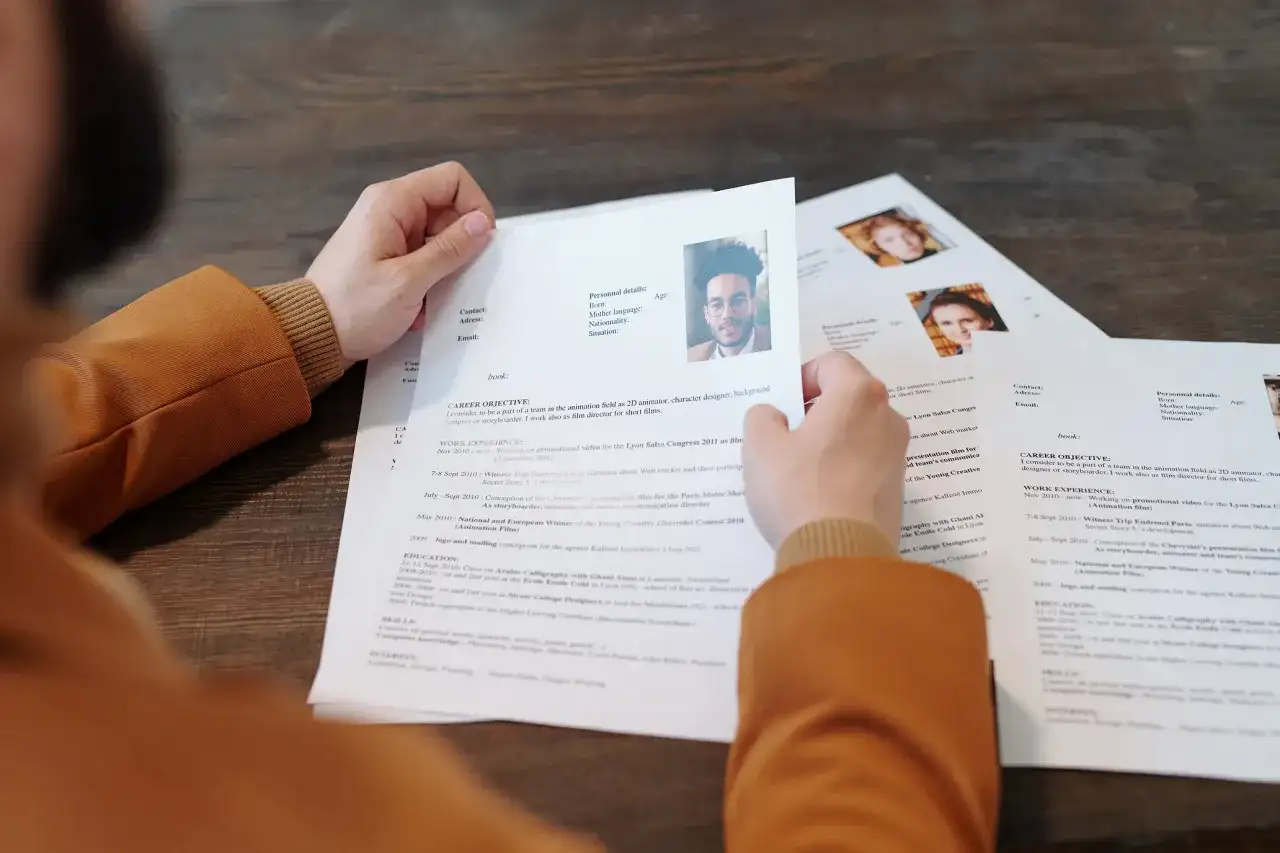 Osoba przegląda dokumenty CV z portretami.