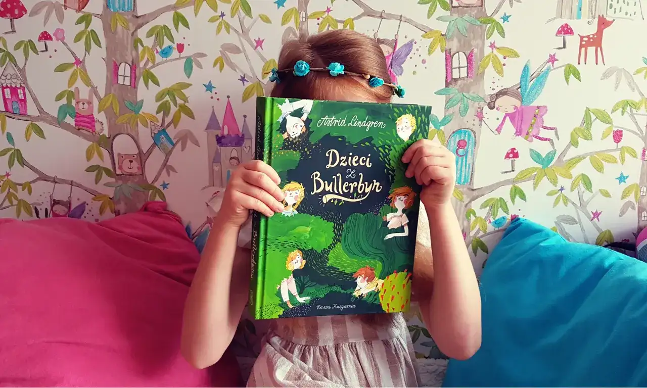 Dziecko z książką "Dzieci z Bullerbyn", której autorem jest Astrid Lindgren, na tle bajkowej tapety.