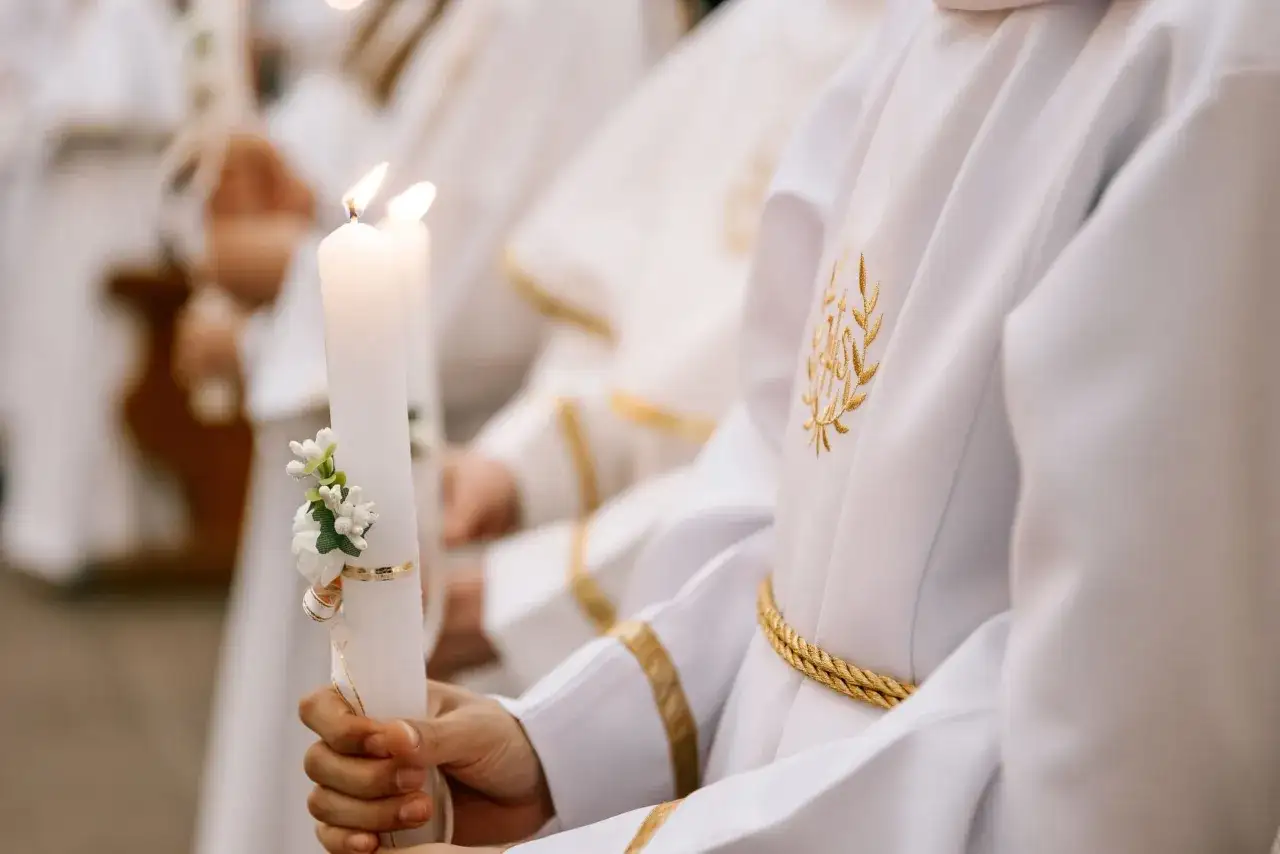 Dziecko trzyma ozdobioną świecę podczas komunii. Zastanawiasz się, ile kosztuje komunia na 30 osób?