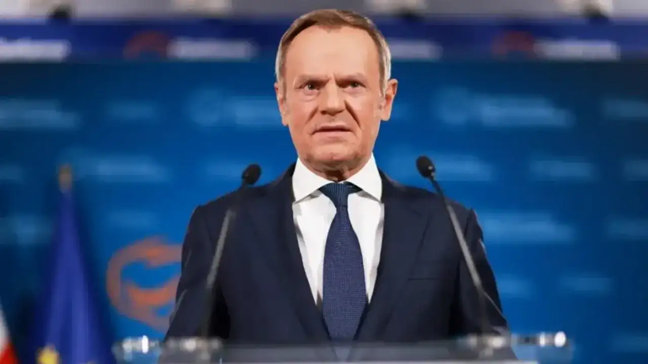 Donald Tusk w garniturze przemawia przy mównicy z mikrofonami.