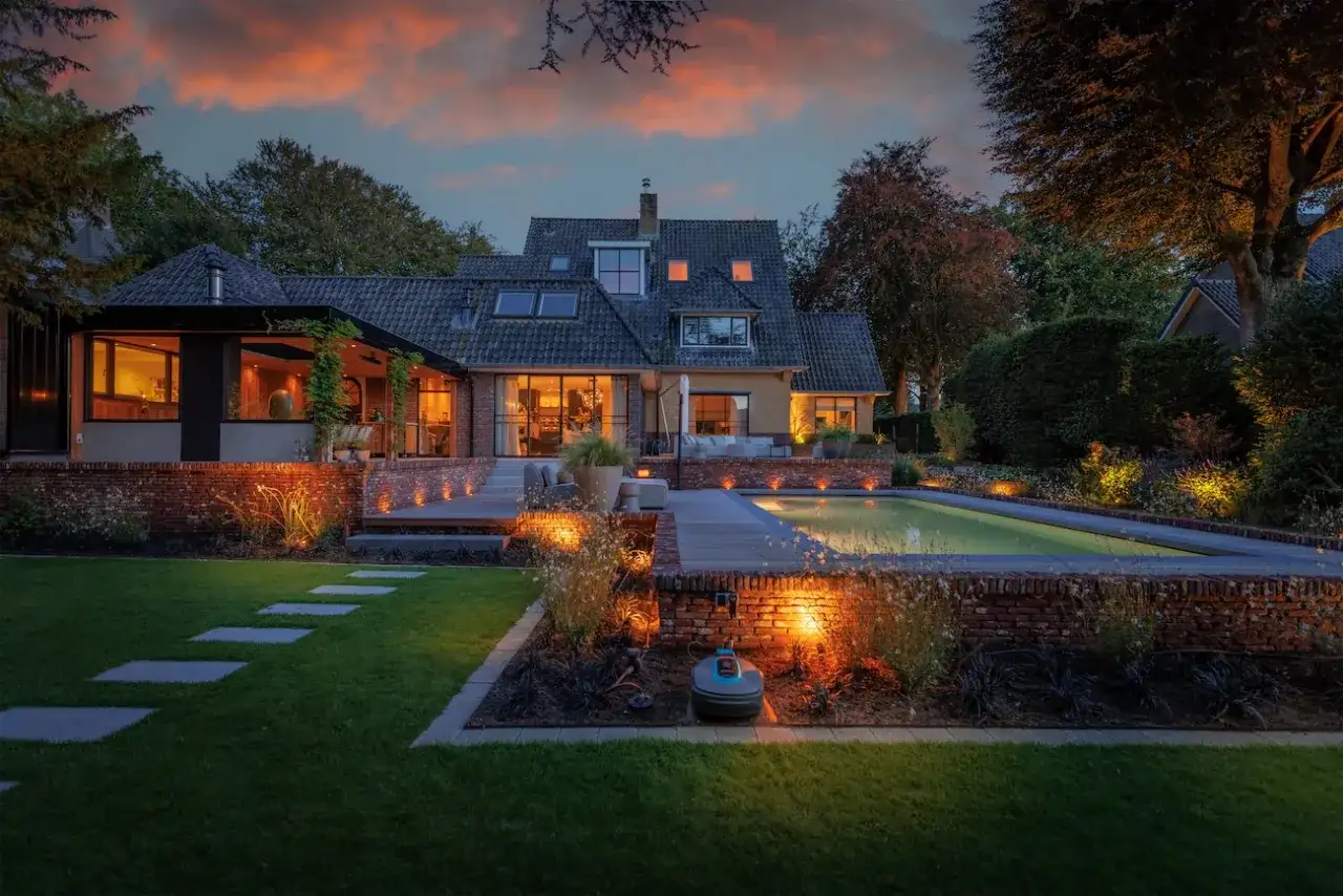 Piękny dom z basenem i tarasem, oświetlony ciepłym światłem. Oświetlenie z akumulatora na działce tworzy magiczną atmosferę wieczorem.