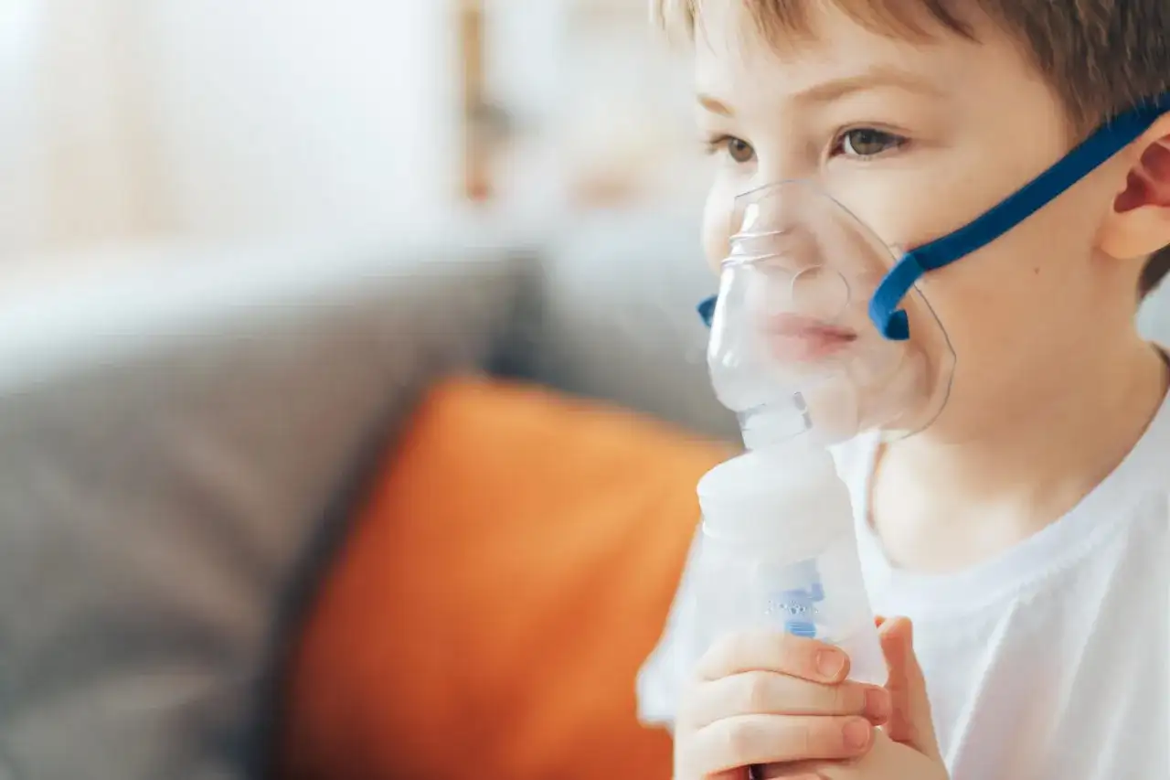 Chłopiec w masce nebulizatora wykonuje inhalację.