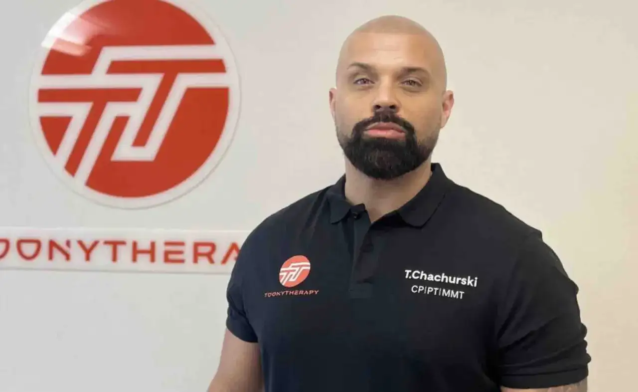 Tomasz Chachurski w czarnej koszulce z logo Toonytherapy, na tle białej ściany.