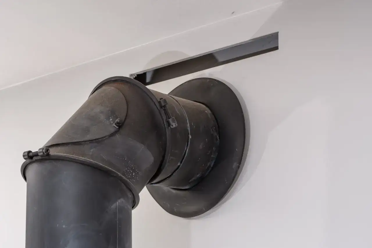 Czarny, metalowy komin z kolankiem, podłączony do pieca na drewno. Zastanawiasz się, jaka średnica komina do pieca na drewno będzie najlepsza?