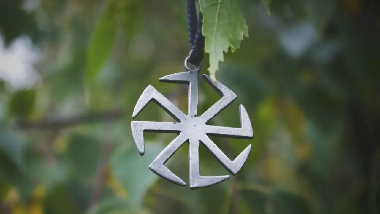 Metalowy symbol Słońca, jeden z wielu symbole słowiańskie znaczenie. Wisi na sznurku wśród zielonych liści.