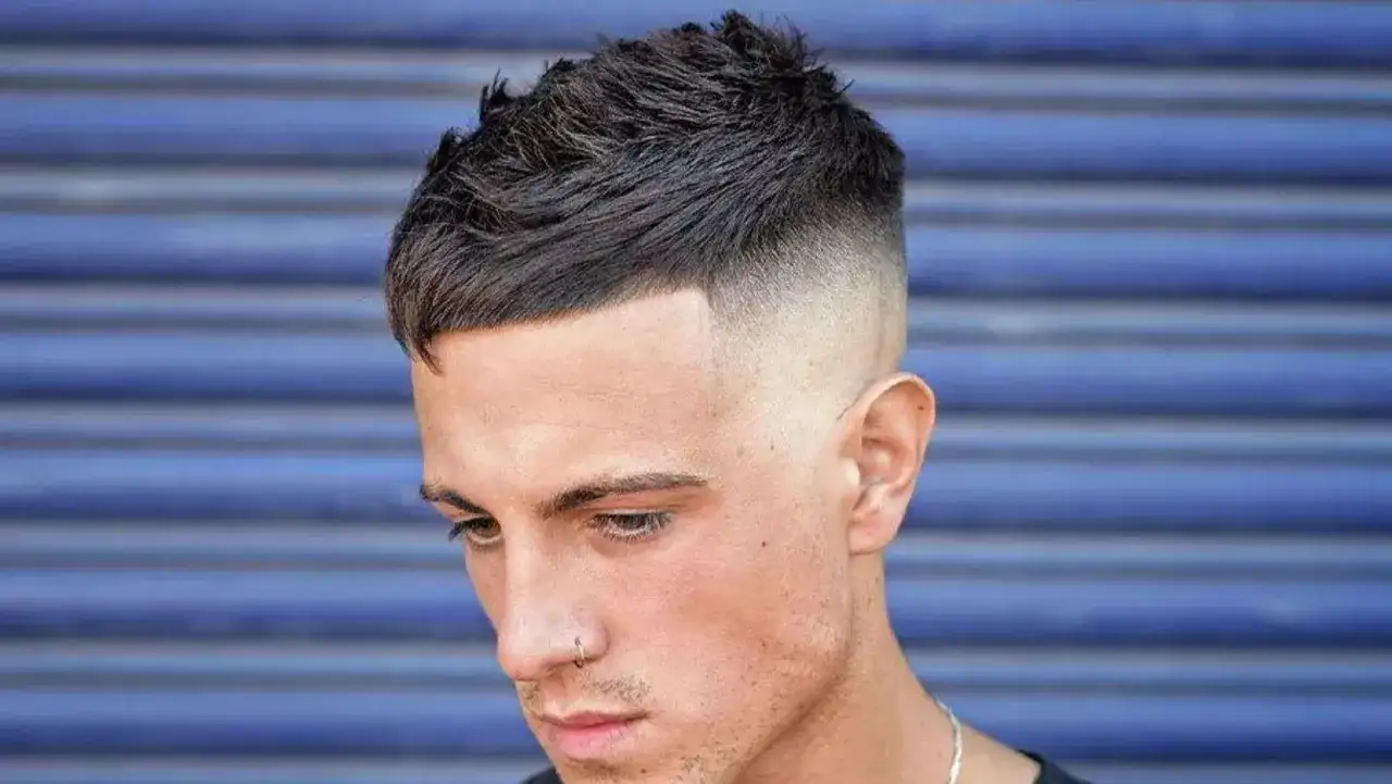 Mężczyzna z wysokim czołem i zakolami, z modną fryzurą typu crop z cieniowanymi bokami.