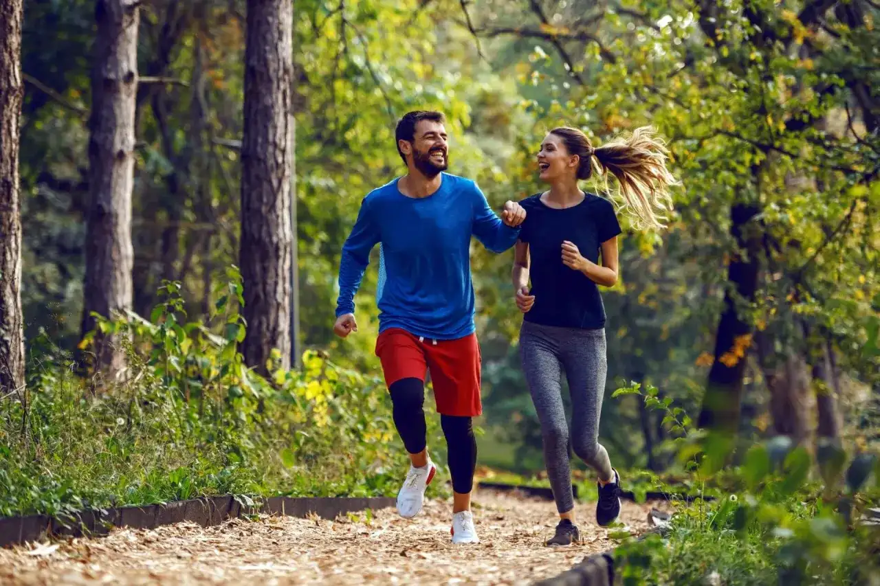 Szczęśliwa para cieszy się wspólnym trail run w jesiennym lesie.