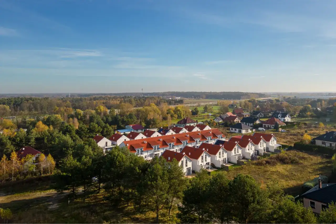 Osiedle domów z czerwonymi dachami, otoczone drzewami. Zdjęcia z drona ukazują jesienny krajobraz.
