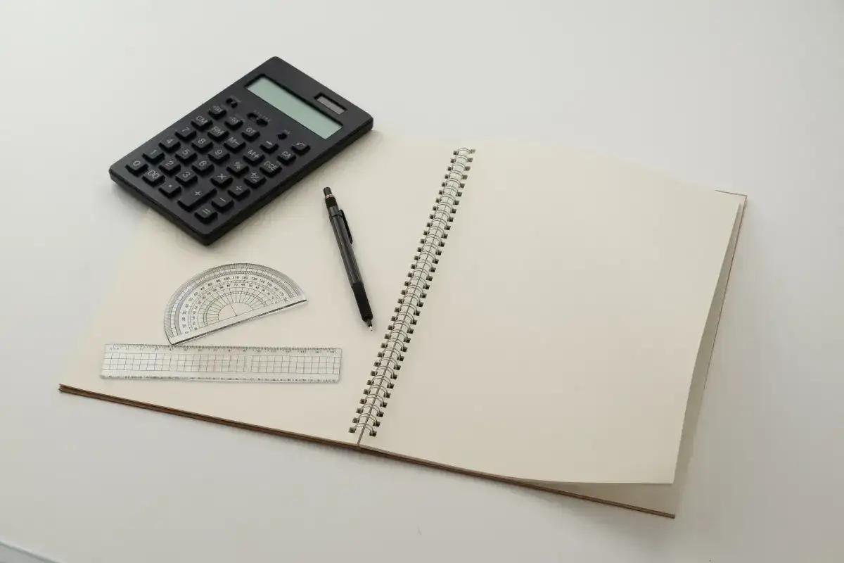 Kalkulator, ołówek, linijka i kątomierz na otwartym notatniku.