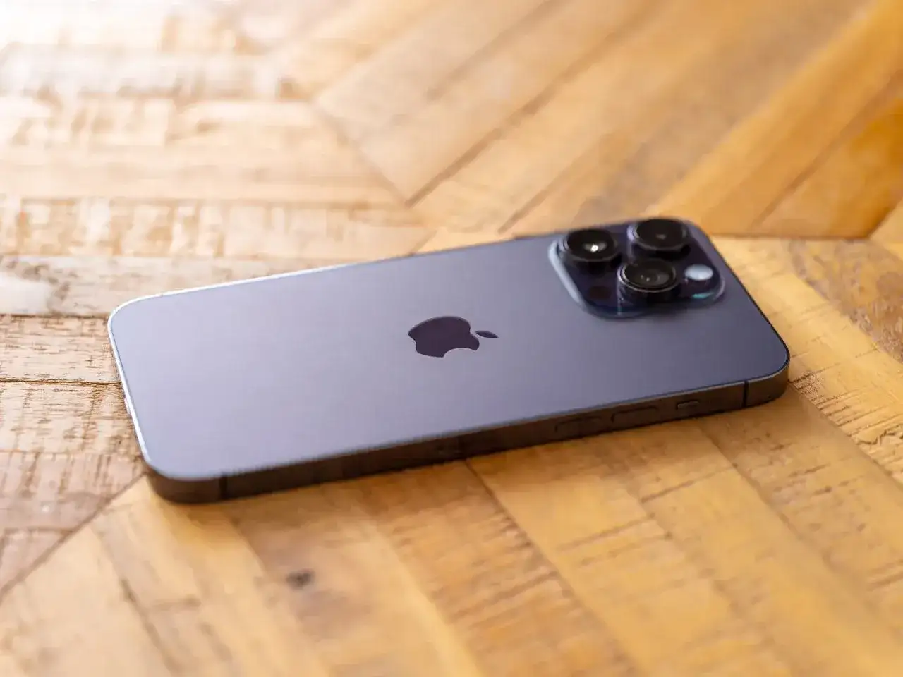 Nowy iPhone 14 Pro Max aparat z trzema obiektywami na drewnianym tle.