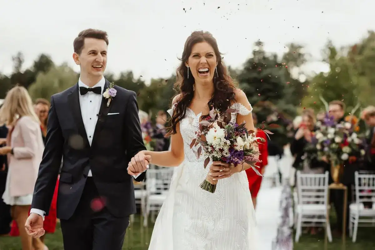 Szczęśliwa para młoda idzie alejką, obsypana płatkami. Zastanawiasz się, o co pytać fotografa na wesele?