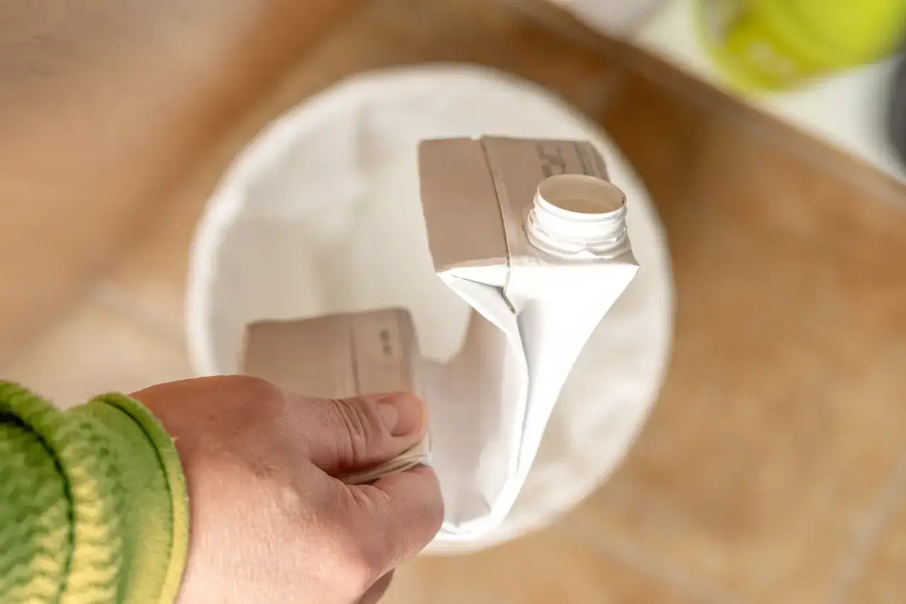 Ręka trzyma pusty karton po mleku, gotowa do wyrzucenia. Pytanie brzmi: gdzie wyrzucić karton po mleku?