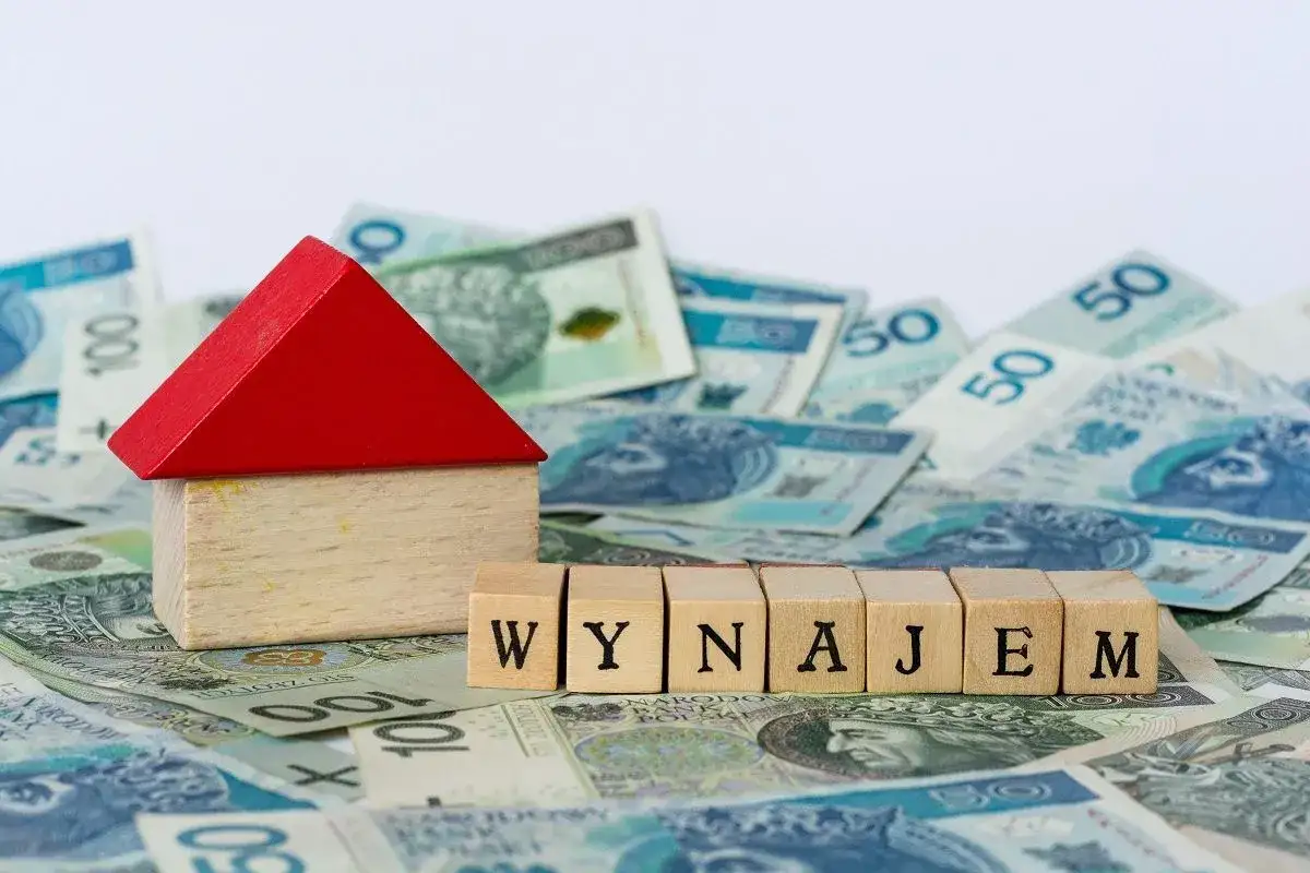 Drewniany domek i kostki z napisem "WYNAJEM" na tle polskich banknotów. Zgłoszenie umowy najmu do urzędu skarbowego.