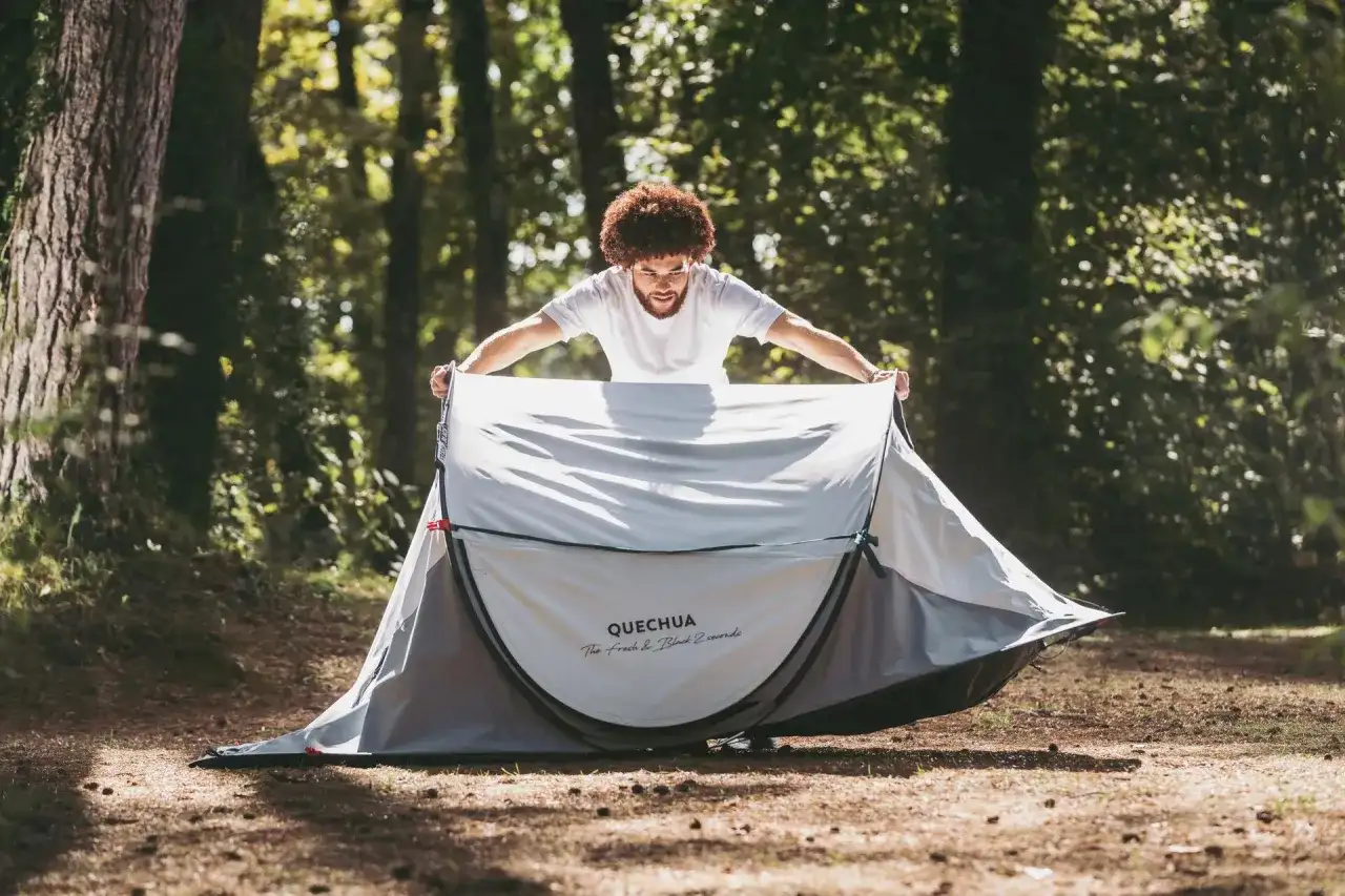 Mężczyzna rozkłada namiot Quechua w lesie.