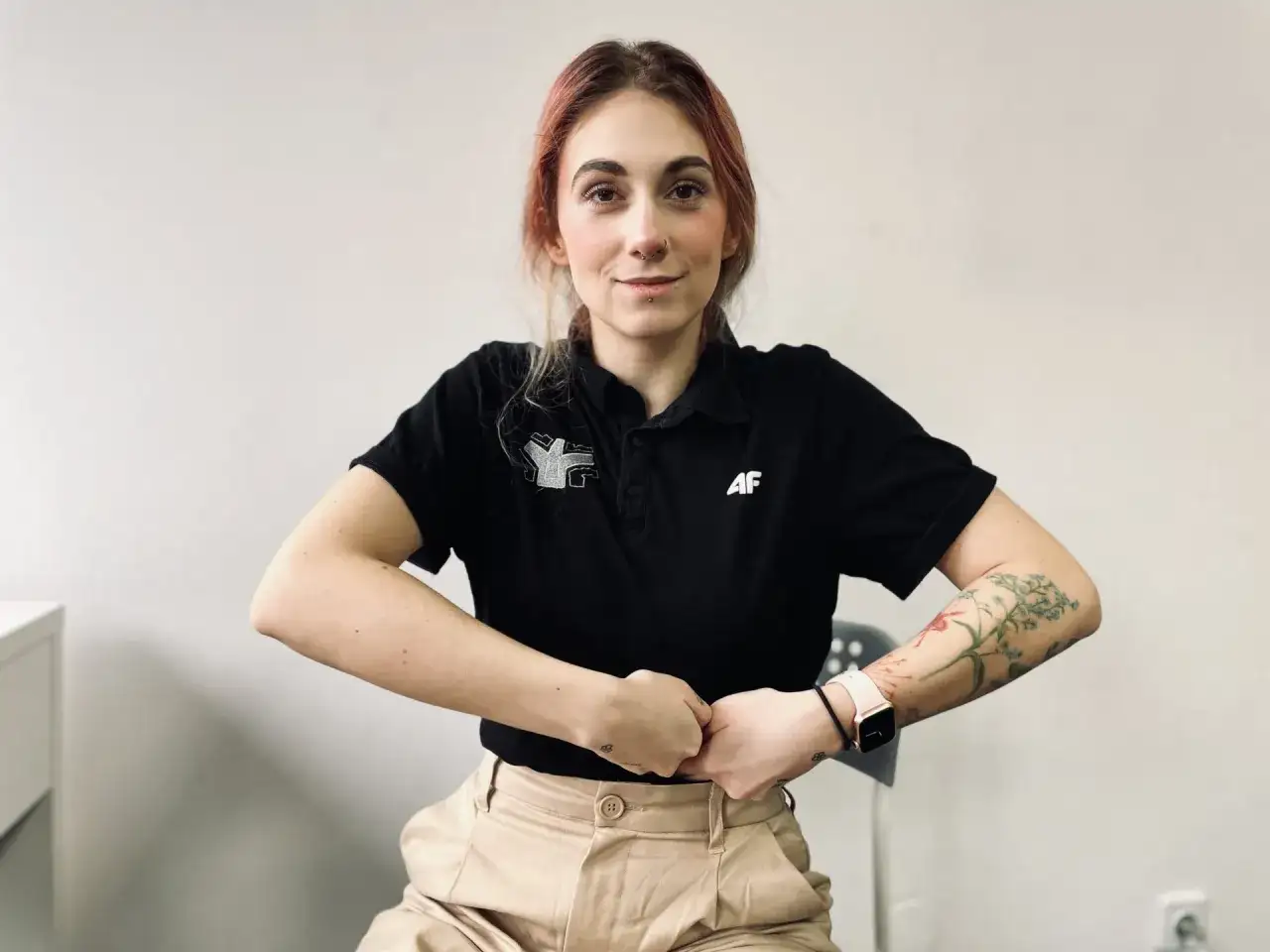 Kobieta w czarnej koszulce i beżowych spodniach trzyma ręce na brzuchu.