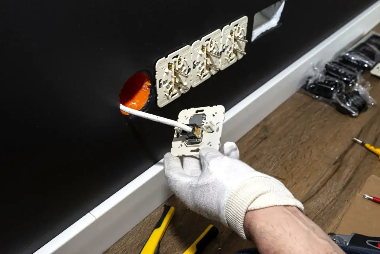 Instalacja gniazdek elektrycznych. Ręka w białej rękawiczce podłącza przewód do mechanizmu gniazdka. W ścianie widać już kilka zamontowanych gniazdek. Zastanawiasz się, ile za punkt elektryczny?