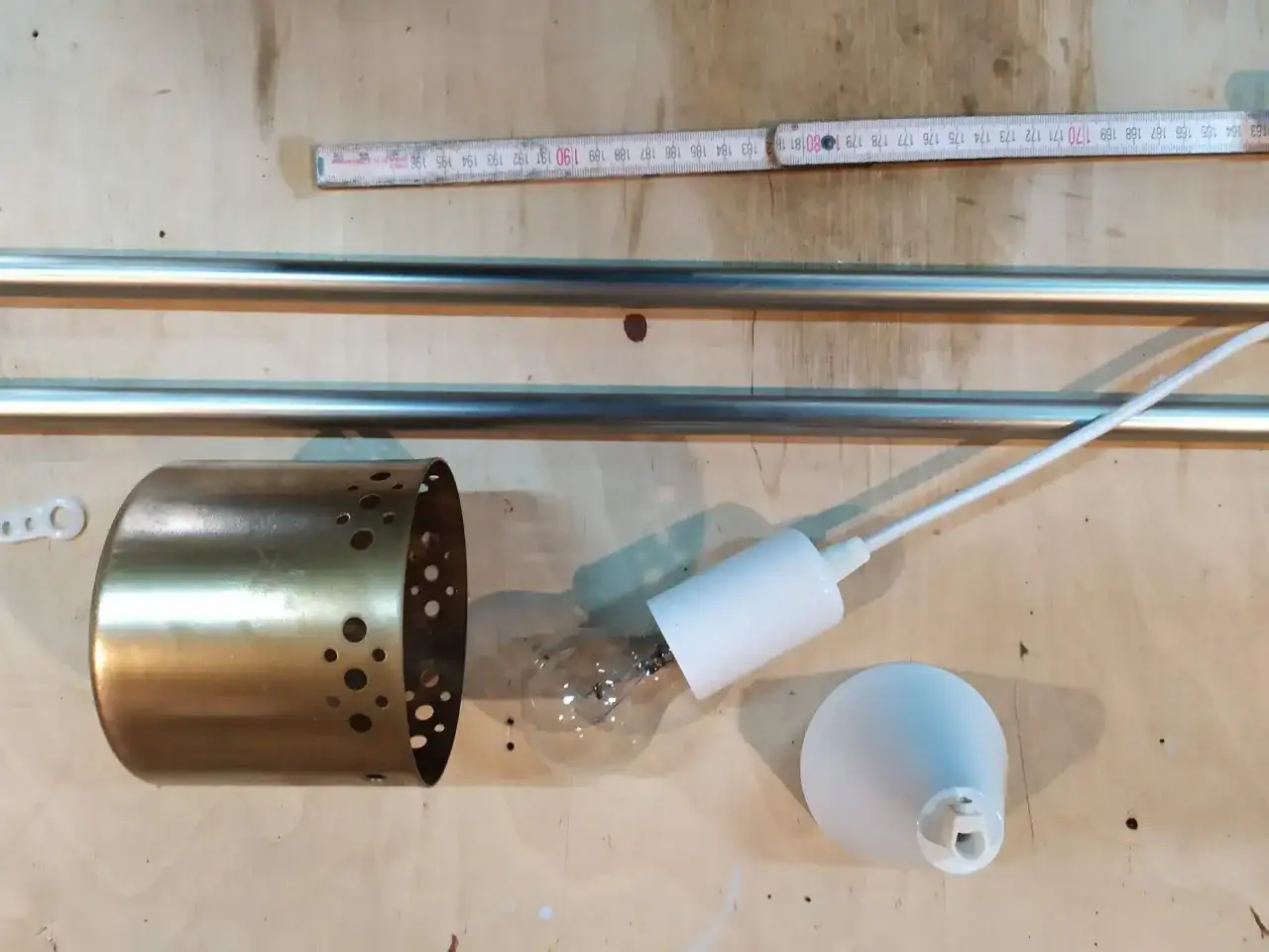 Elementy do zrobienia lampy wiszącej: metalowa osłona, żarówka, biały uchwyt i biała podsufitka.