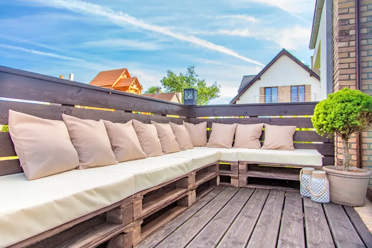 Wygodny taras z palet z beżowymi poduszkami, idealny na letnie wieczory.
