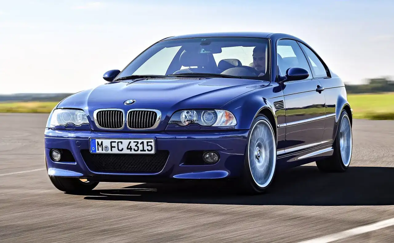 Niebieskie BMW M3 E46, ikona motoryzacji z lat produkcji 2000-2006, pędzi po drodze.