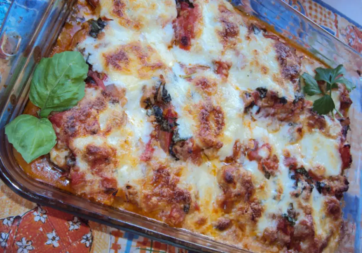 Zapiekanka z cukinii i mięsa mielonego z roztopionym serem i bazylią w szklanym naczyniu.