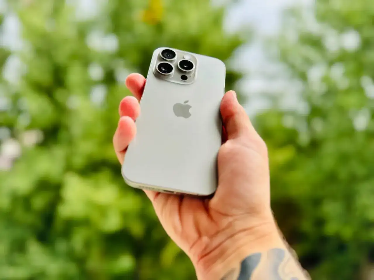 Dłoń trzyma srebrny iPhone 15 Pro Max, prezentując jego potężny aparat.