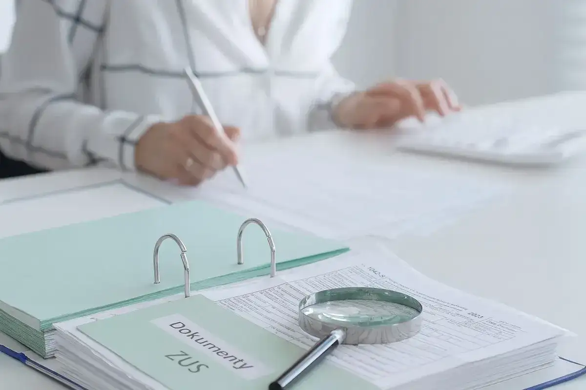 Dokumenty ZUS, lupa i osoba pisząca na klawiaturze.