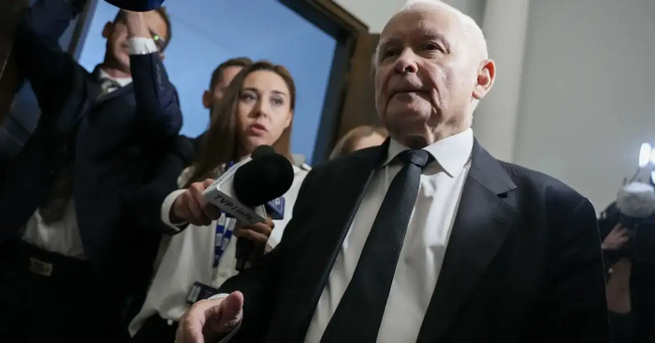 Starszy mężczyzna w garniturze, otoczony przez dziennikarzy z mikrofonem TVP Info, być może odpowiada na pytanie: co złego zrobił PiS?