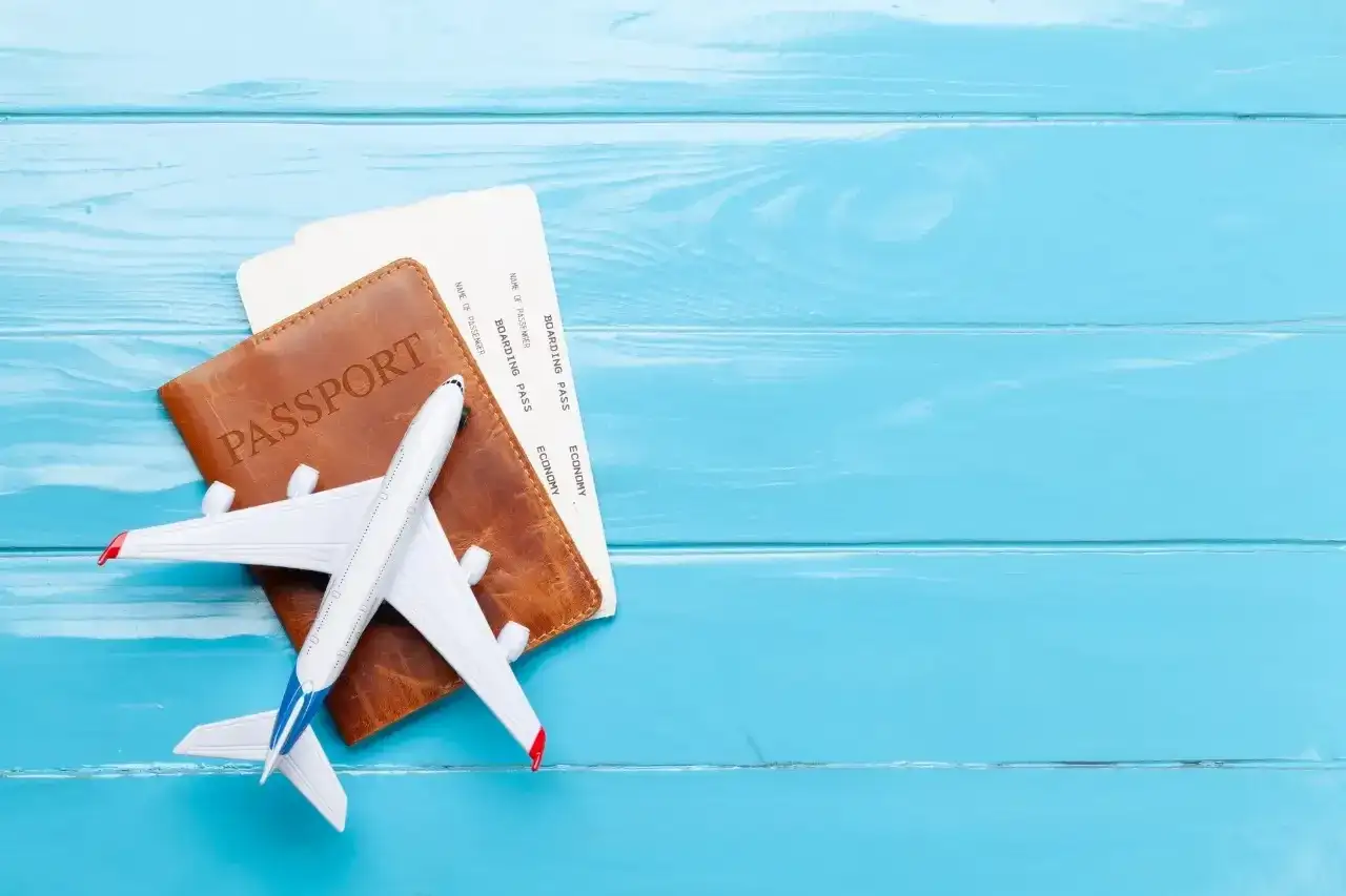 Paszport, bilety lotnicze i model samolotu na niebieskim tle. Sprawdź, jakie dane do biletu lotniczego są potrzebne do podróży.