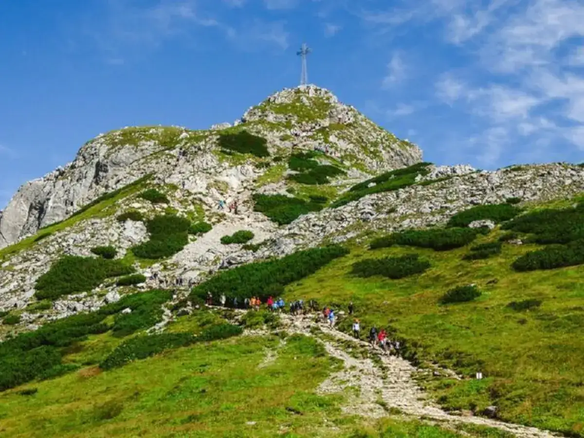 Grupa turystów wspina się kamienistym szlakiem na szczyt Giewontu w Tatrach. Góra przypomina śpiącego rycerza.