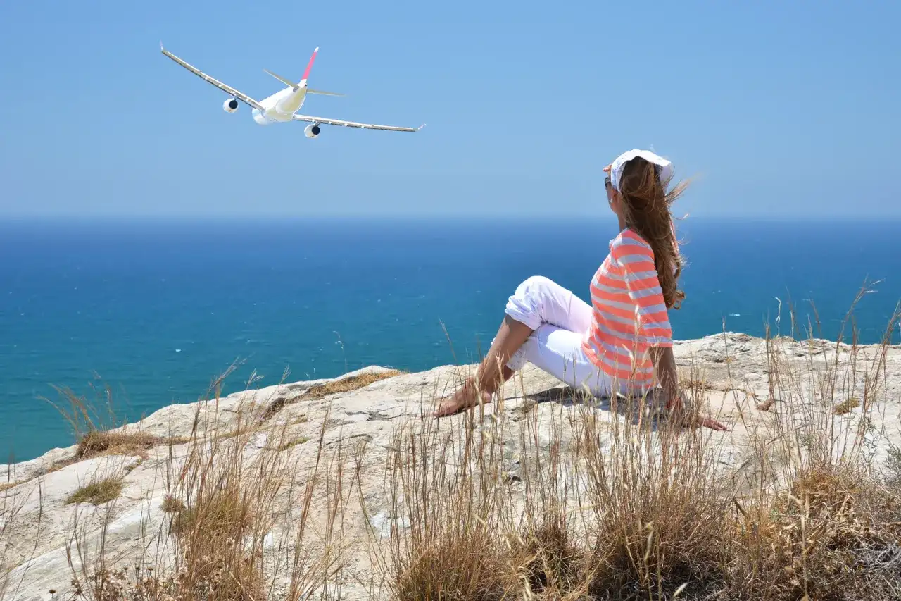 Kobieta siedzi na klifie, patrząc na samolot wznoszący się nad morzem. Widok na port lotniczy Larnaka.