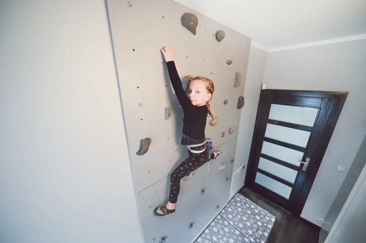 Dziewczynka wspina się po domowej ściance wspinaczkowej. To świetny sposób, by pokazać, jak zrobić ściankę wspinaczkową dla dzieci.