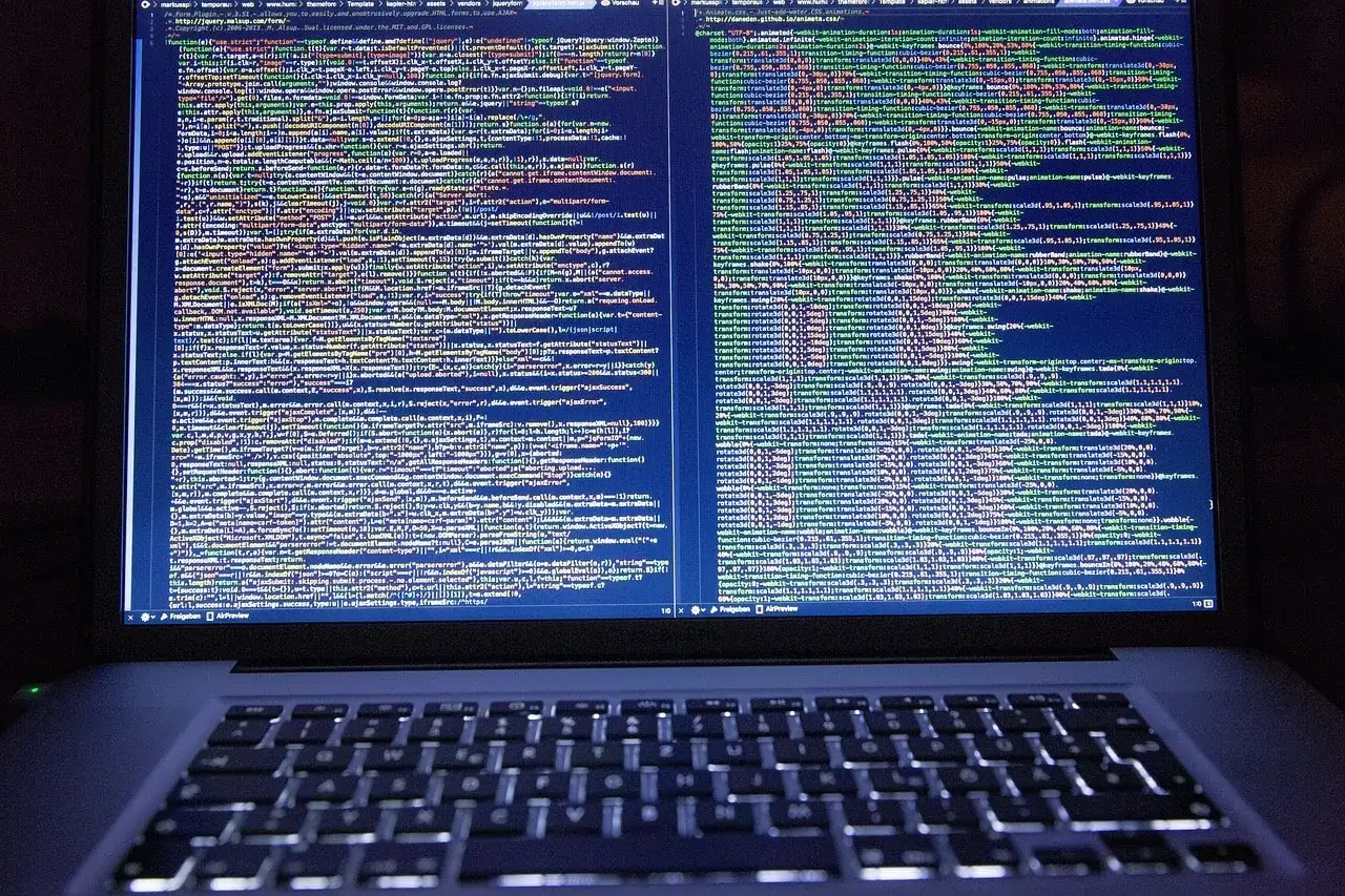 Kod źródłowy na ekranie laptopa pokazuje, jak zrobić odnośnik do strony HTML. Widać fragmenty kodu JavaScript i CSS.